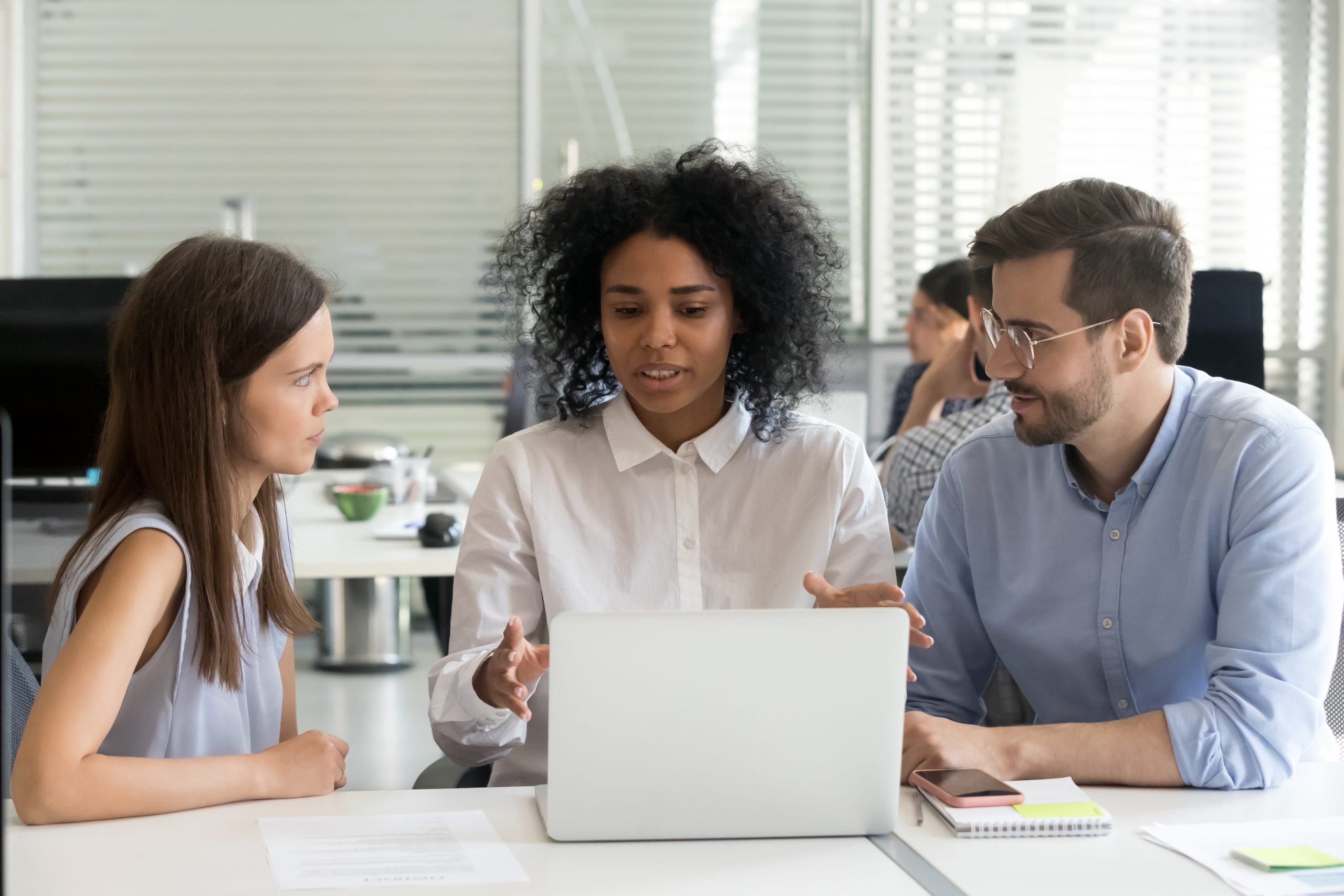 Diverse workers sitting at desk in coworking open space, african american leader at the head of team. Black skilled employee coach teaching newcomers interns explaining about new corporate application